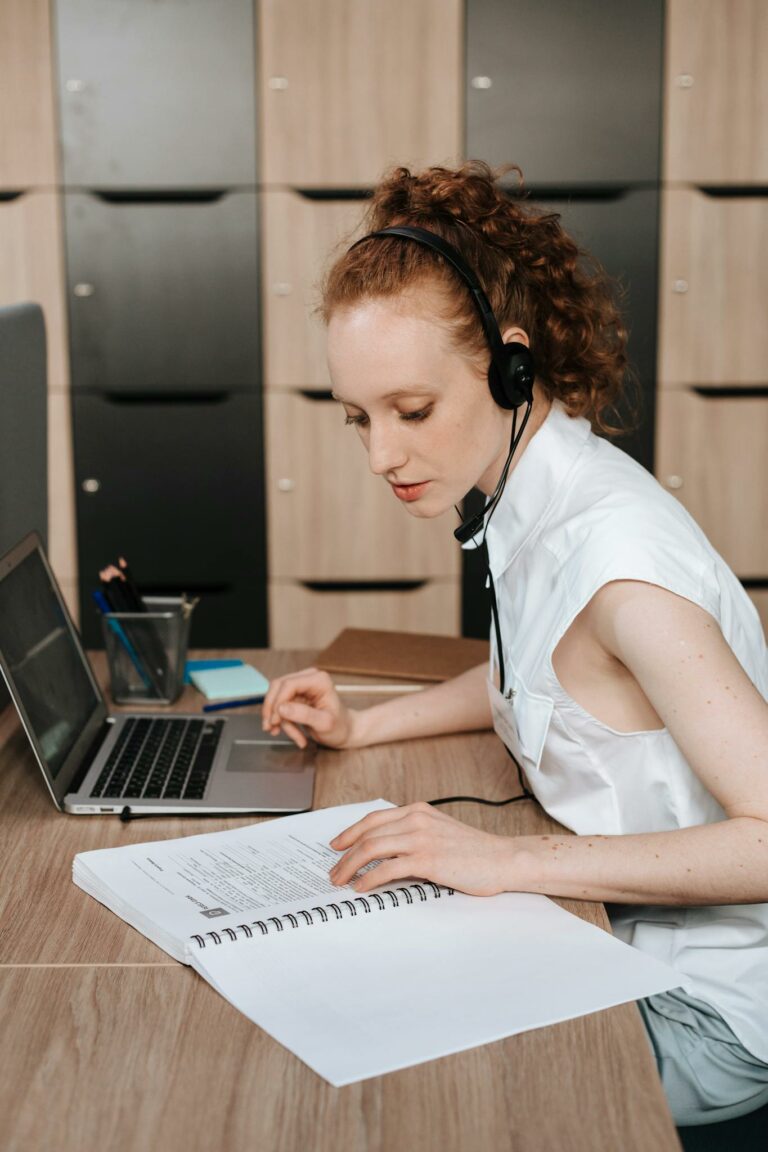 Woman in office working remotely with laptop and headset, focused on online learning or meeting.